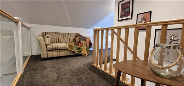 the landing space with glass balustrade, striped 2 seater sofa and wooden bannisters by the stairs